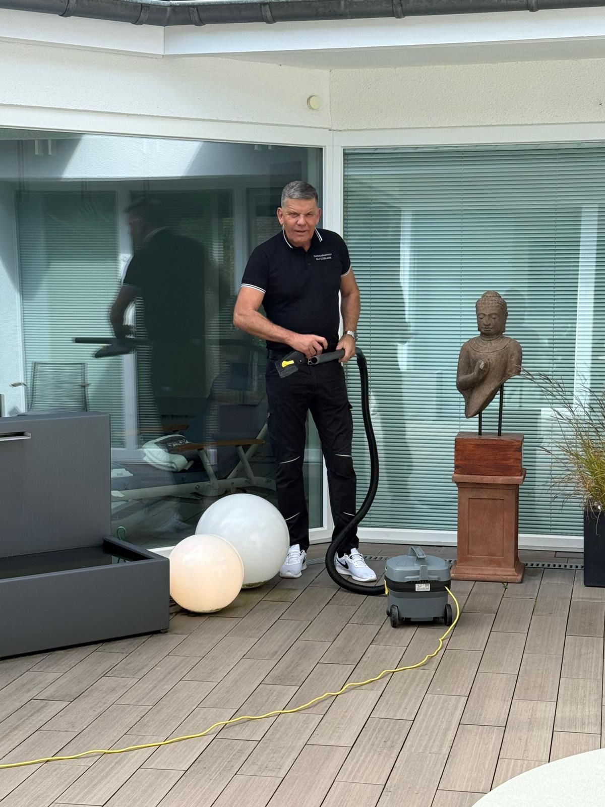 Jürgen Plogmann im Firmen-Poloshirt saugt eine Terrasse mit dem Kärcher-Sauger